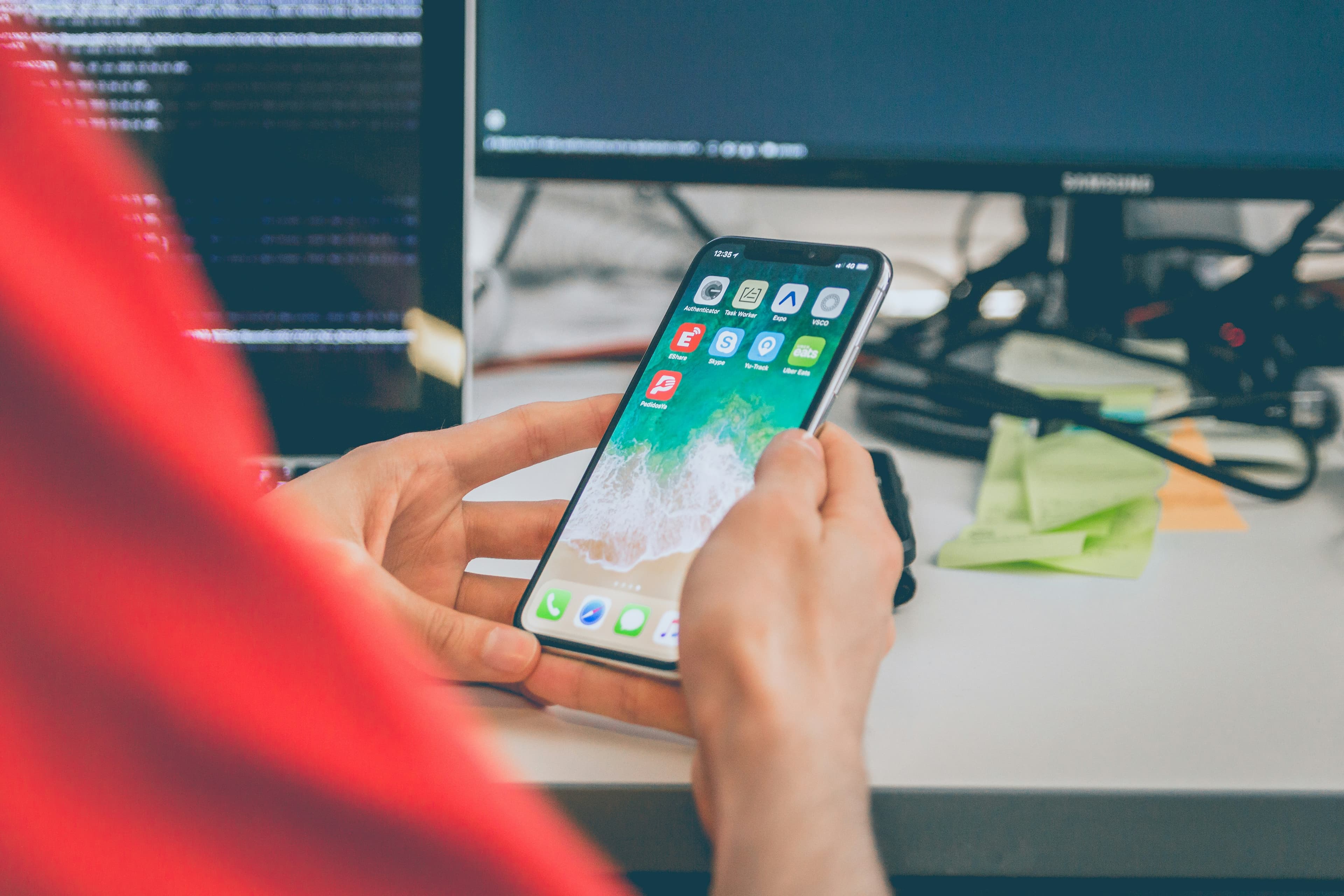 Person holding a smartphone in front of application code on a monitor