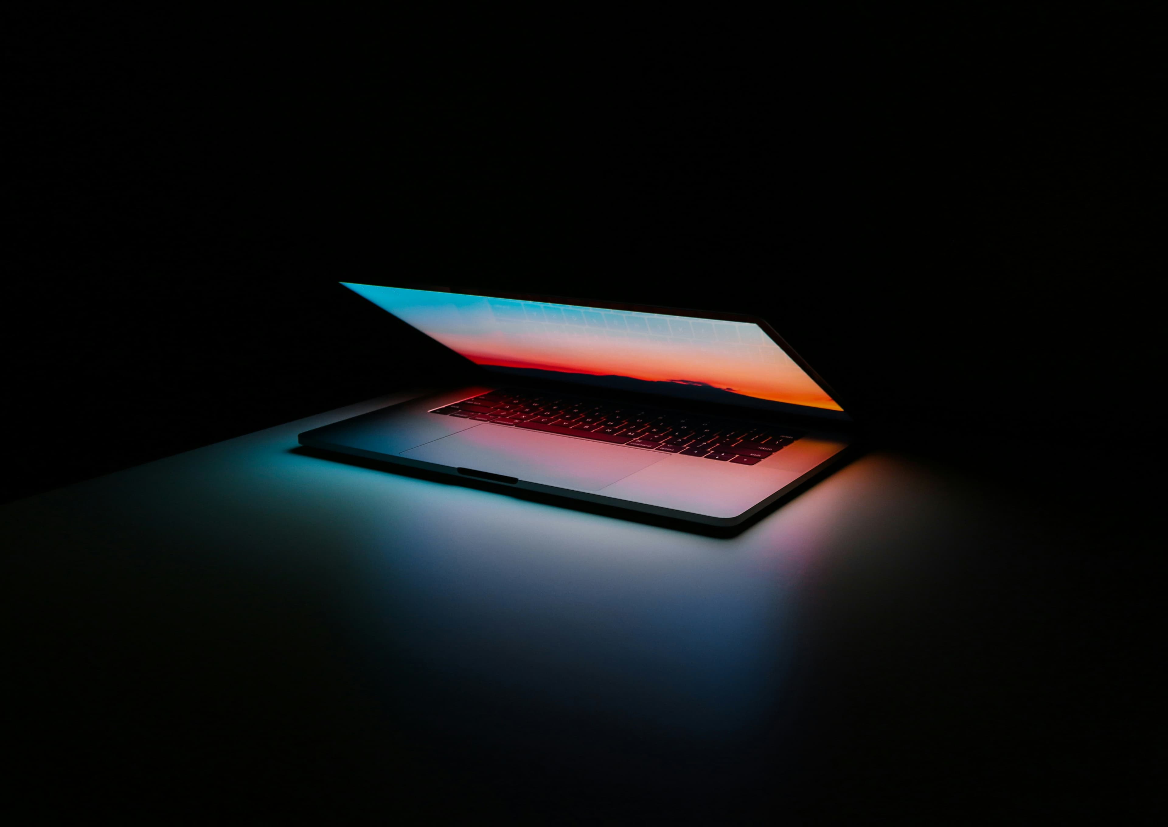 Laptop illuminated by cyan and red light in a dark workspace